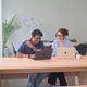 Two colleagues working at a table and smiling in a light, modern office space