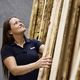 A woman in a black polo shirt examines wooden planks stacked vertically in a workshop or warehouse.