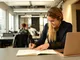 A woman writing in a note book while sitting in front of a computer