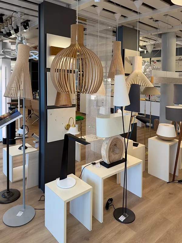Im hell erleuchteten Ausstellungsraum von Lichthaus Melzer mit Holzboden werden verschiedene moderne Pendel- und Stehlampen in Holz- und Metallausführung präsentiert.