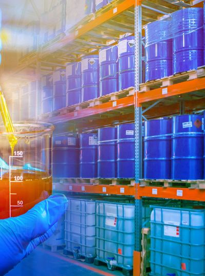 Viscous liquid in a laboratory glass jar in front of a high-bay warehouse with barrels