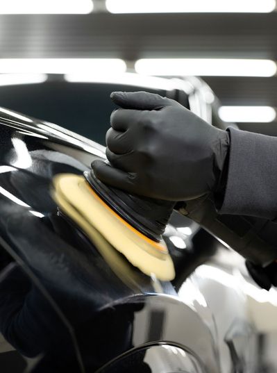 Person polishing a black car with a power buffer in a garage