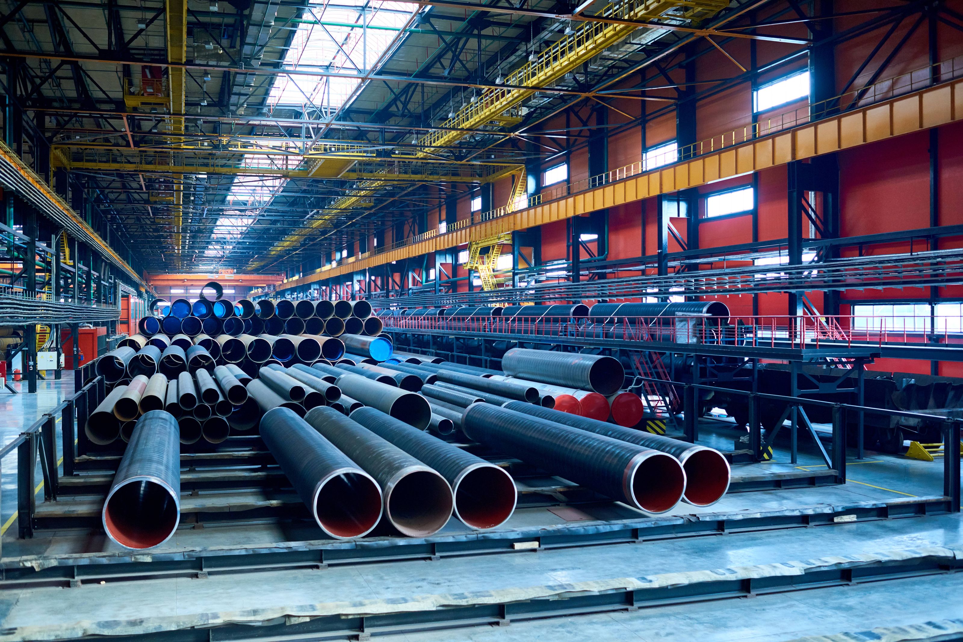 Interior of a large industrial warehouse with stacks of metal pipes
