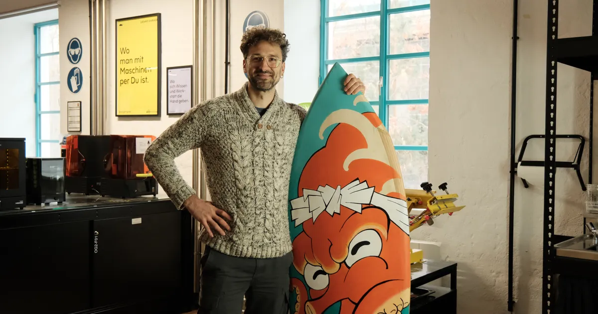 Foto eines Makers im Makerspace der sein selbst gebautes Surfboard hält