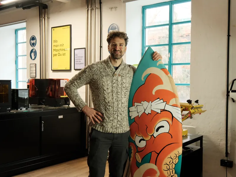Foto eines Makers im Makerspace der sein selbst gebautes Surfboard hält
