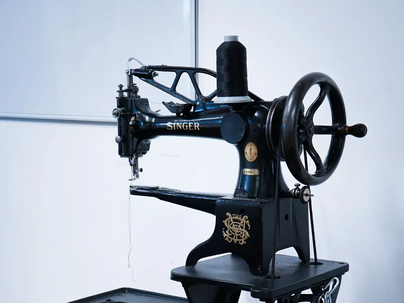 Vintage Singer sewing machine with intricate ironwork, pedal, and spool of black thread, set against a plain background.