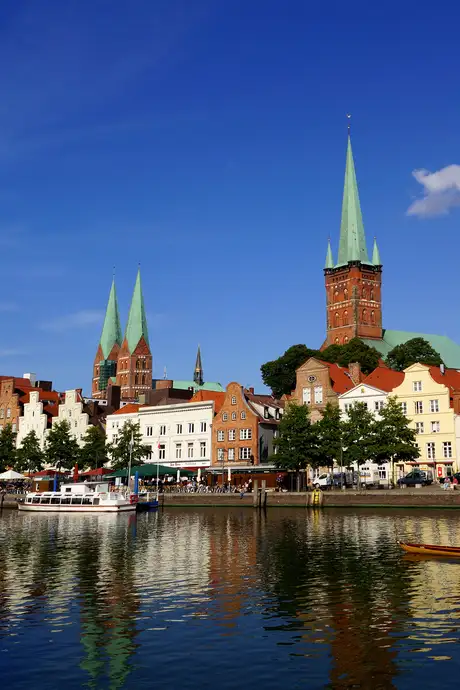 Scenic view of a waterfront town with historic buildings, two tall church spires, and a clear blue sky reflecting in the calm water.