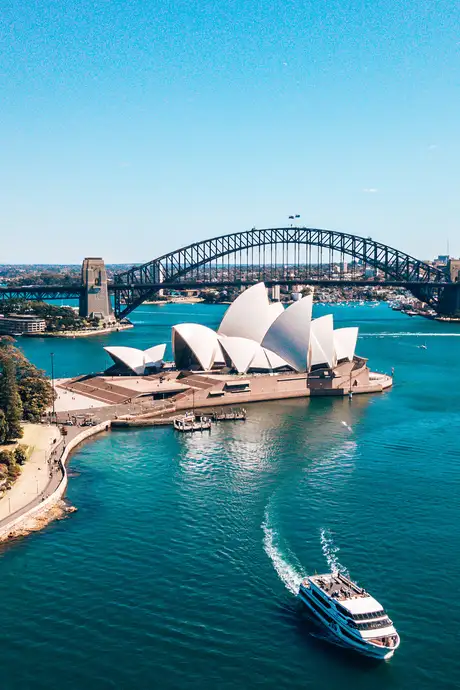 Aerial view of the Sydney Opera House and Sydney Harbour Bridge, with a ferry sailing in the blue water under a clear sky.