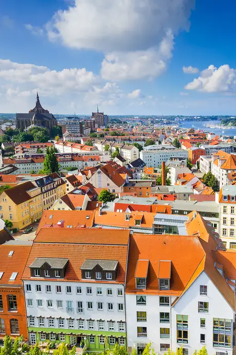 Aerial view of a European town with colorful rooftops, historic buildings, and a church under a partly cloudy blue sky.