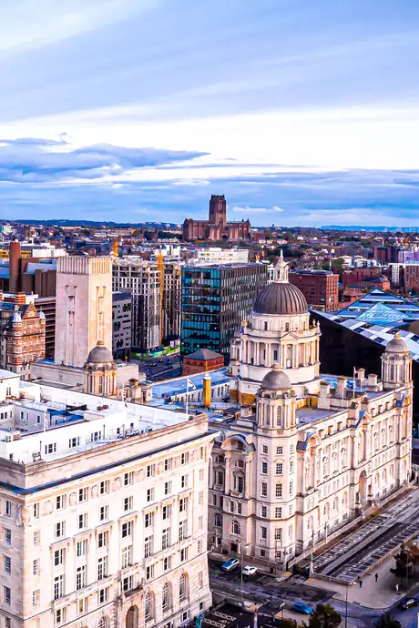 Aerial view of a cityscape featuring historic and modern buildings under a cloudy sky, with a prominent domed structure in the foreground.