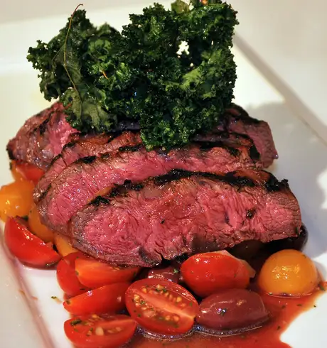 Steak on top of tomatoes and topped with greenery