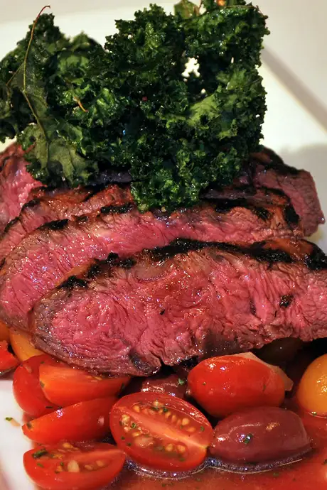 Steak on top of tomatoes and topped with greenery