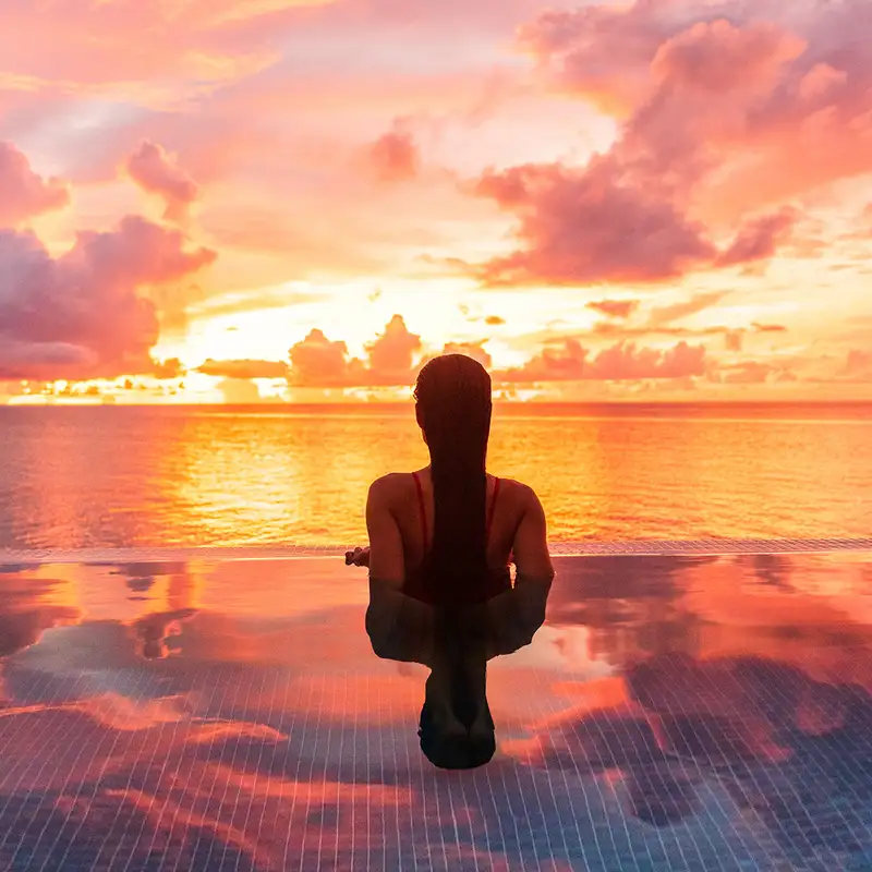 A woman in a pool looking out over the ocean at sunset