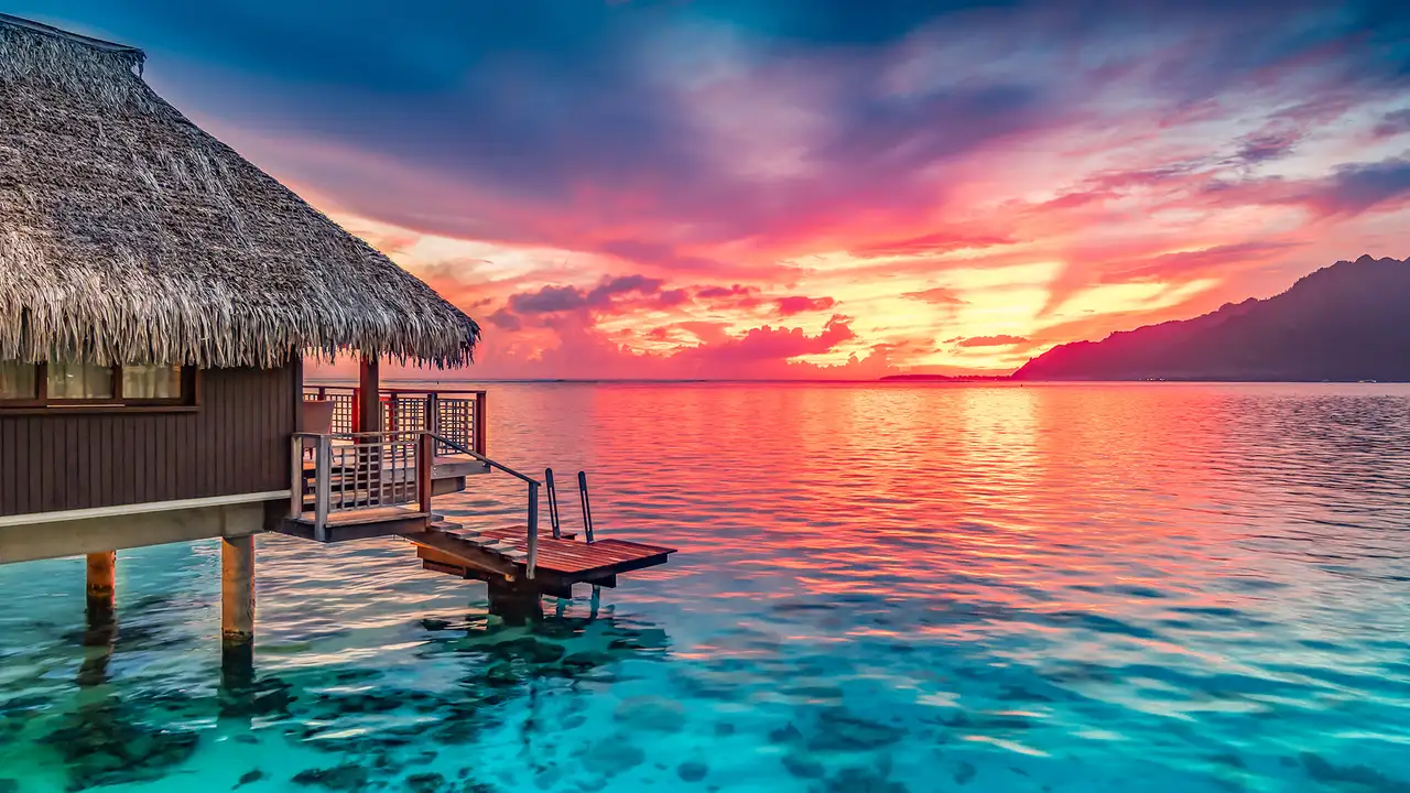 A hut on the ocean facing a sunset in Tahiti