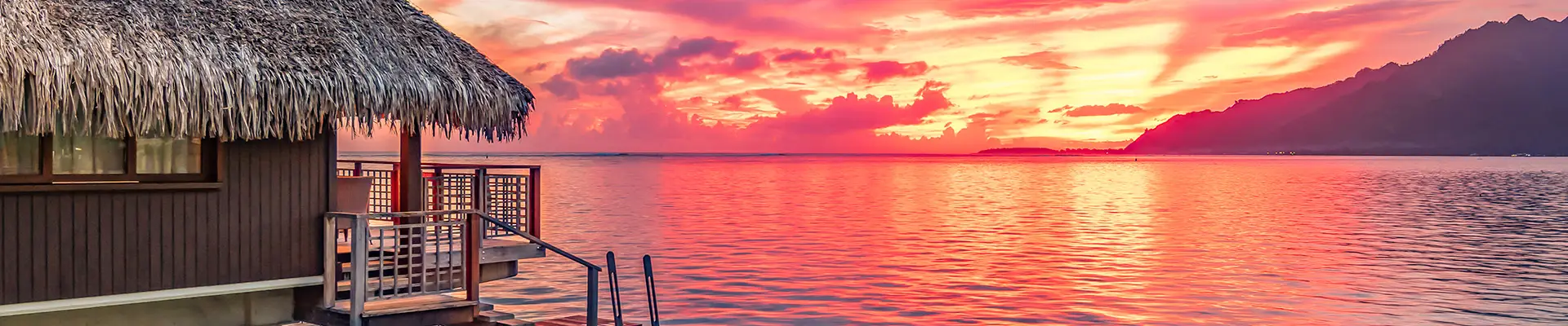 A hut on the ocean facing a sunset in Tahiti
