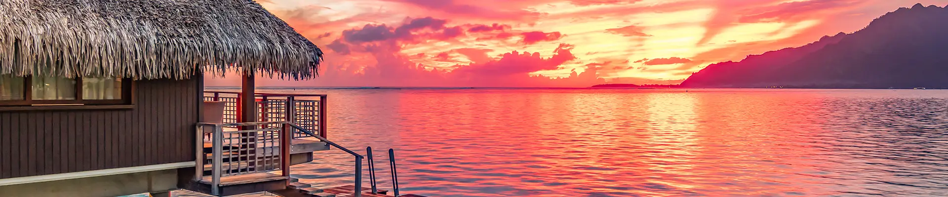A hut on the ocean facing a sunset in Tahiti