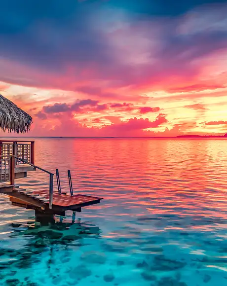 A hut on the ocean facing a sunset in Tahiti