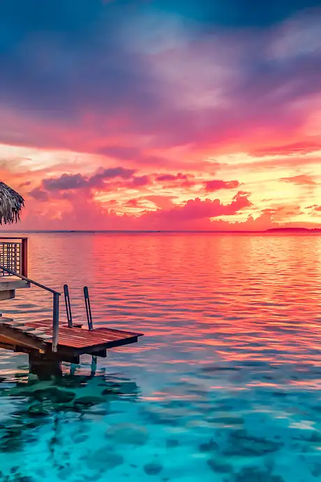 A hut on the ocean facing a sunset in Tahiti