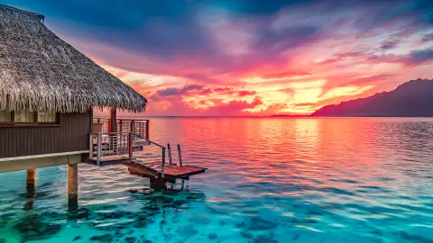 A hut on the ocean facing a sunset in Tahiti