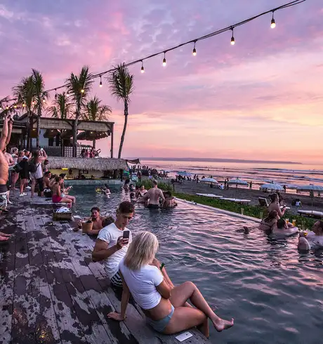 A group of people sitting around a pool at a beach club