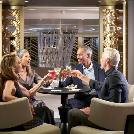 Four people seated around a table raising cocktails in a luxurious setting with golden decor.