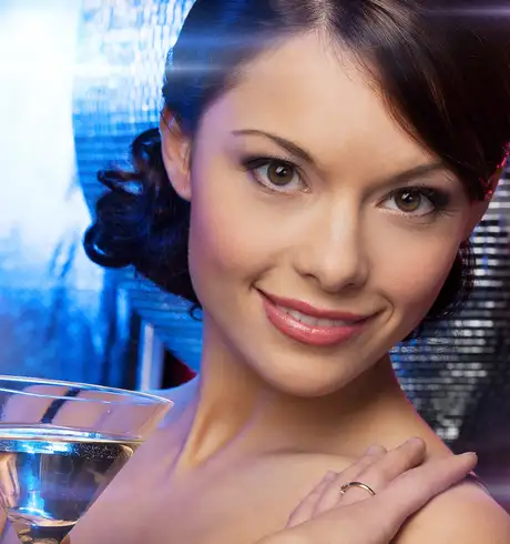 A woman with a drink standing infront of a Disco ball