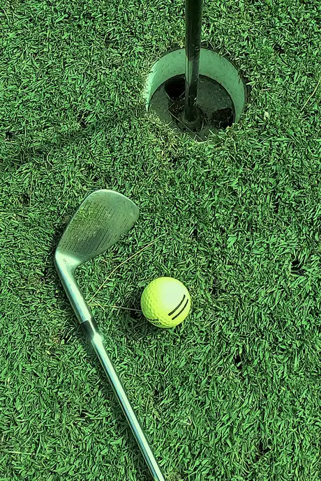 A golf course hole surrounded by a golf club and golf balls