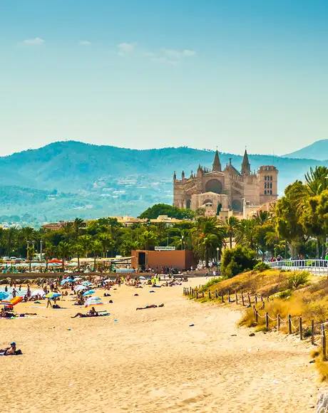 A view of tourists on a sunny beach in Palma with a cathedral and mountains in the distance