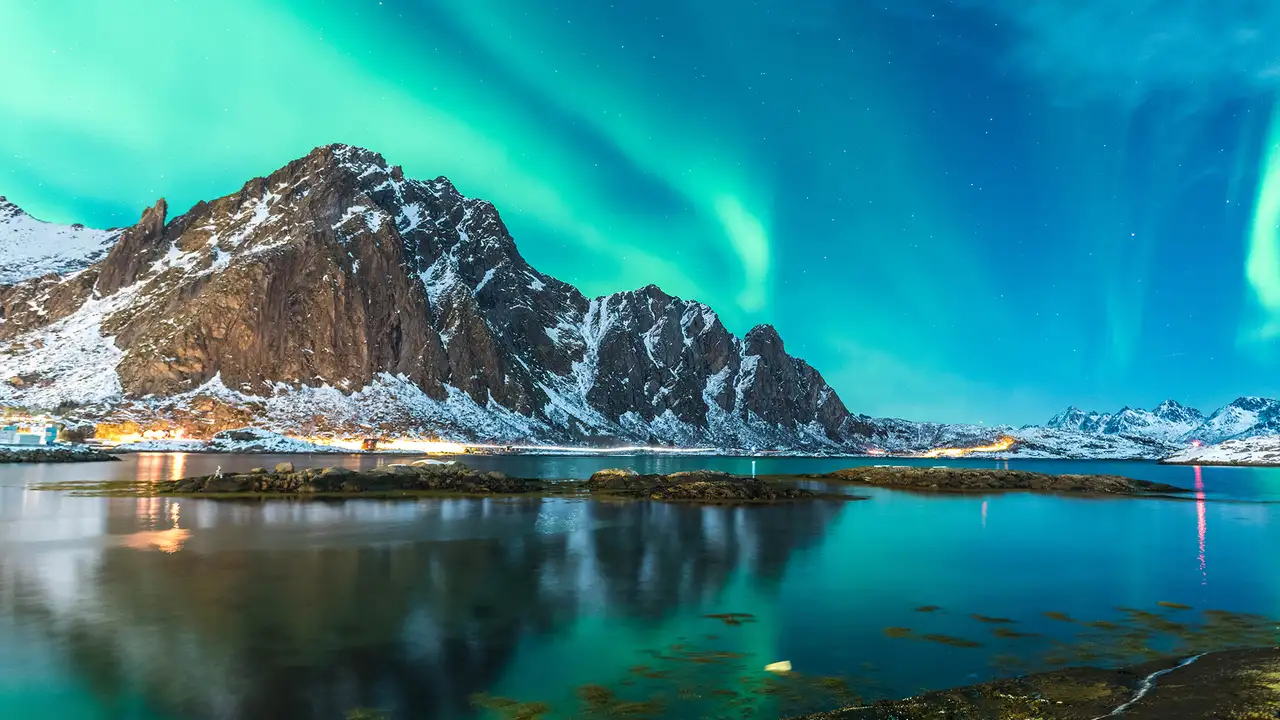 A view of the Northern Lights over a mountain, river and town in Norway