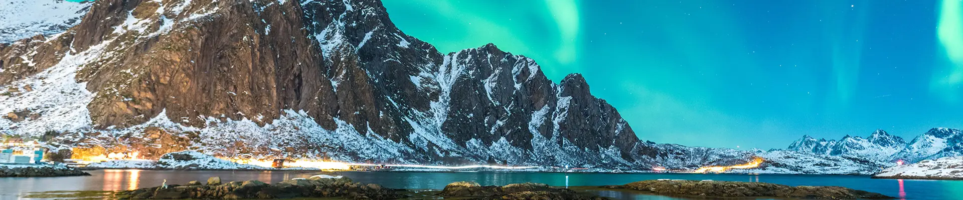 A view of the Northern Lights over a mountain, river and town in Norway