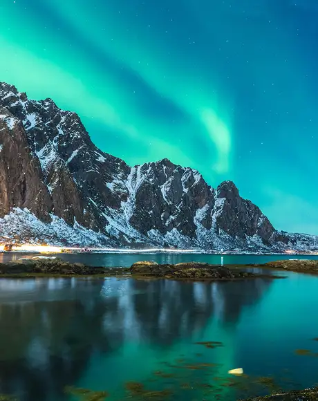 A view of the Northern Lights over a mountain, river and town in Norway