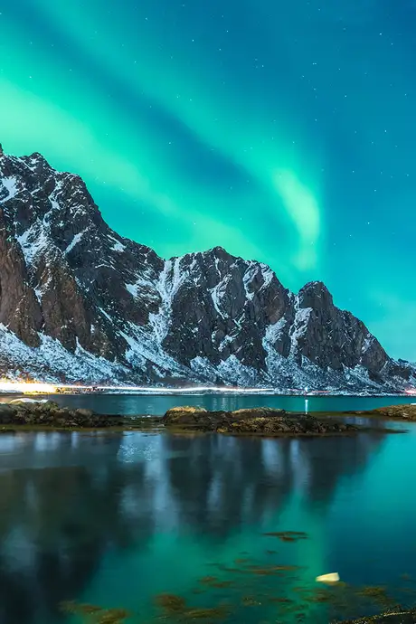 A view of the Northern Lights over a mountain, river and town in Norway