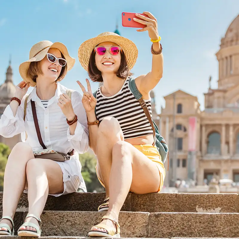 Two Women taking a selfie while sitting one the steps infront of an old building in Barcelona