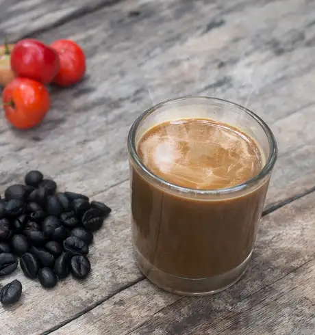 A coffee next to some coffee beans and fruit