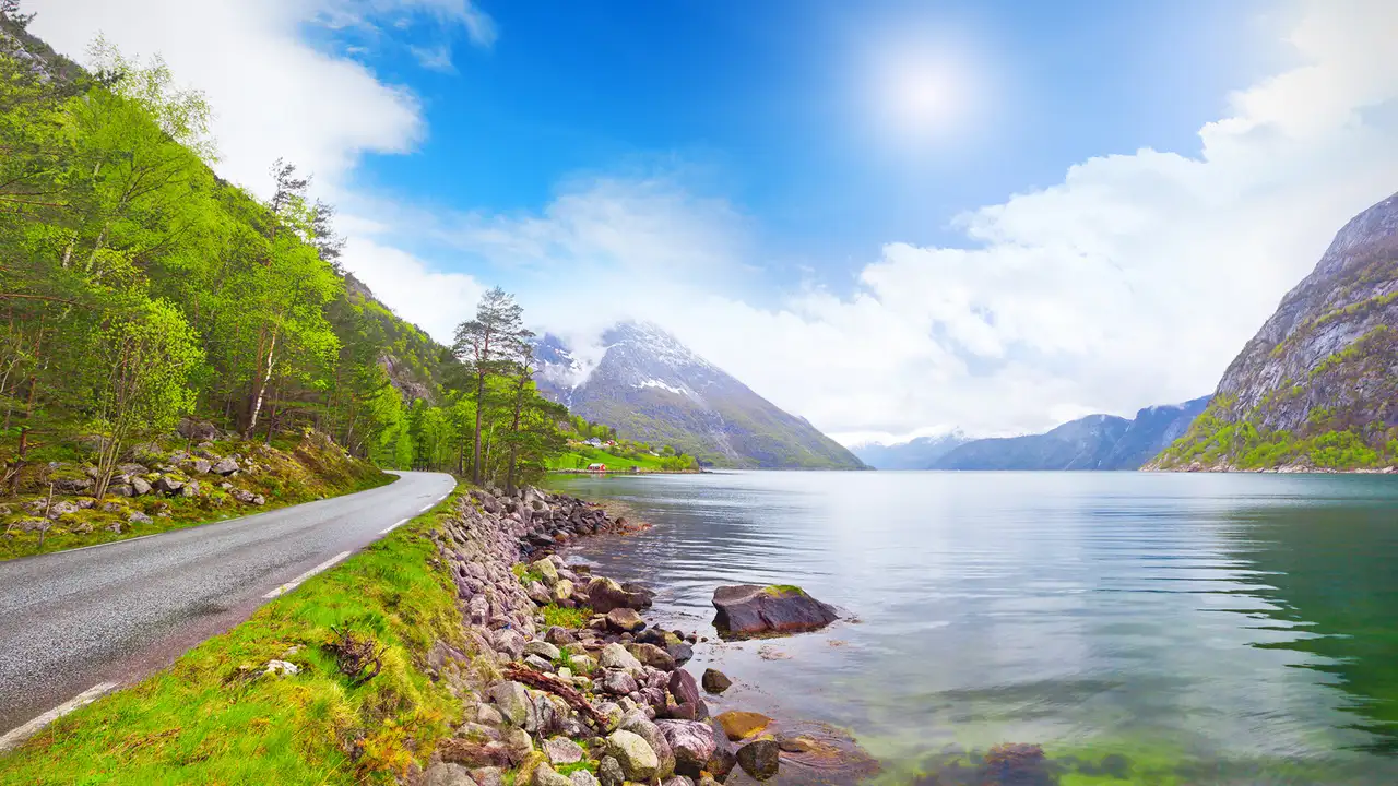 An image of Eidfjord, showing a footpath next to the fjord with mountains in the distance