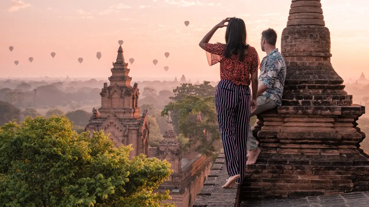 A couple standing on top of a temple watching hot air balloons in the distance