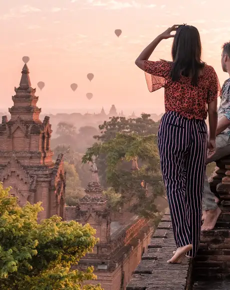 A couple standing on top of a temple watching hot air balloons in the distance