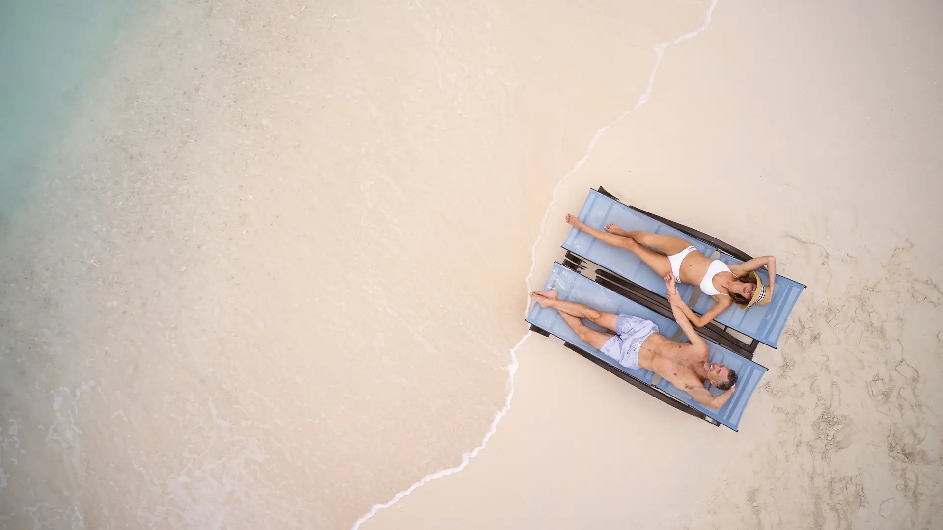 A Couple relaxing in lounge chairs on a beach on Ocean Cay