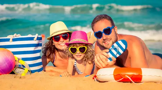 A family at the beach, looking at the camera with matching sunglasses