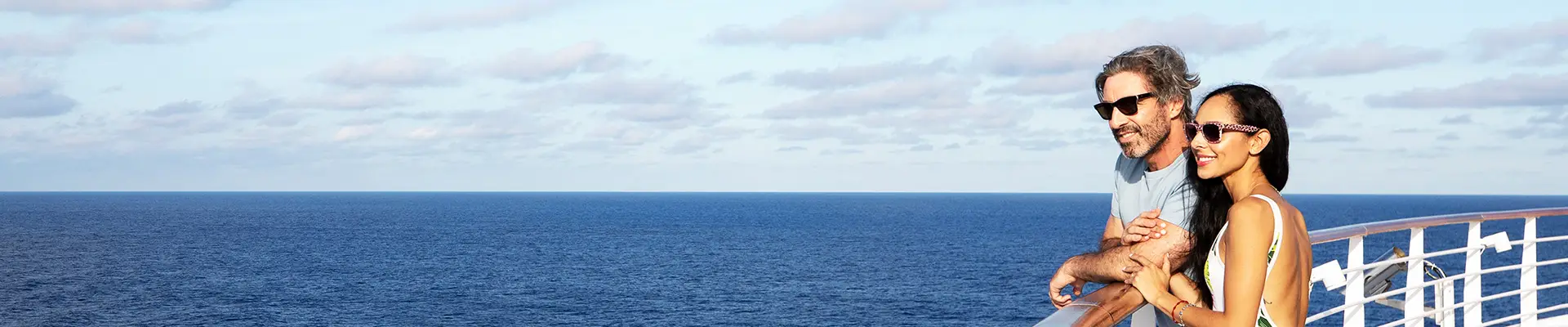 A Couple leaning on a guard rail overlooking the ocean from a Carnival Cruise Ship