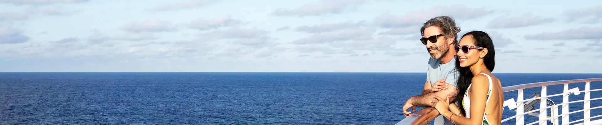 A Couple leaning on a guard rail overlooking the ocean from a Carnival Cruise Ship