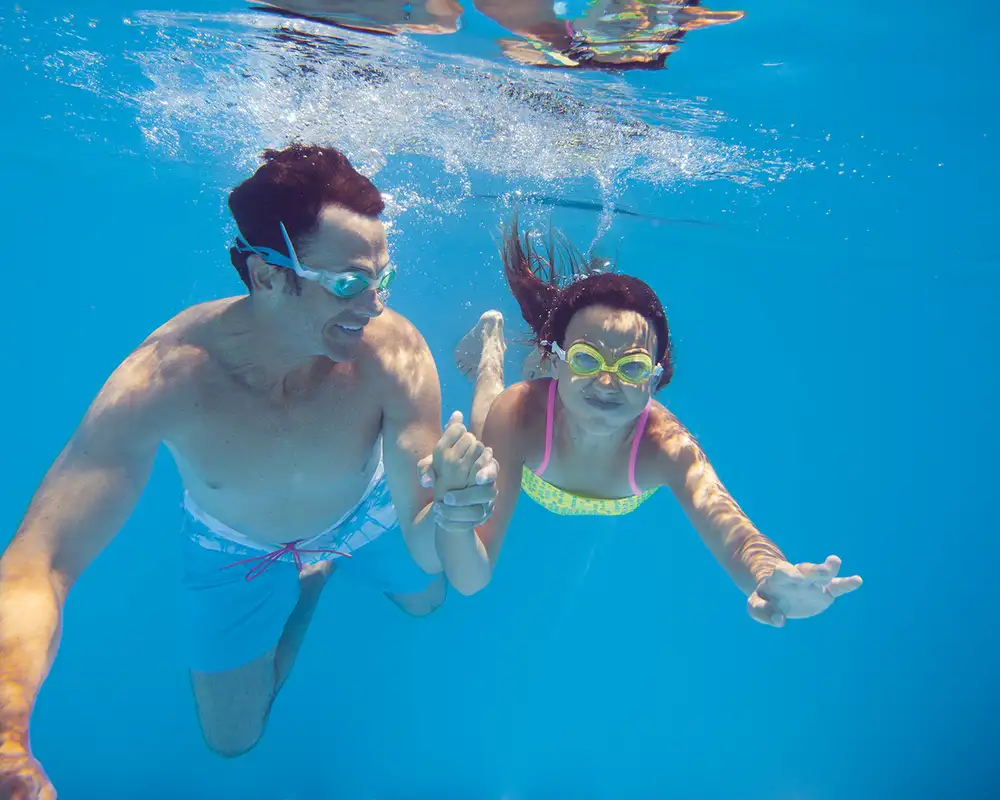 A Father and daughter swimming underwater in a pool on an NCL ship