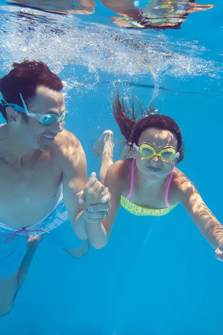 A Father and daughter swimming underwater in a pool on an NCL ship