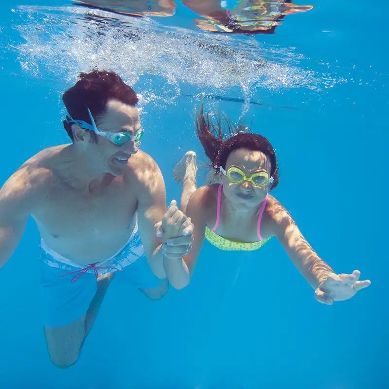 A Father and daughter swimming underwater in a pool on an NCL ship