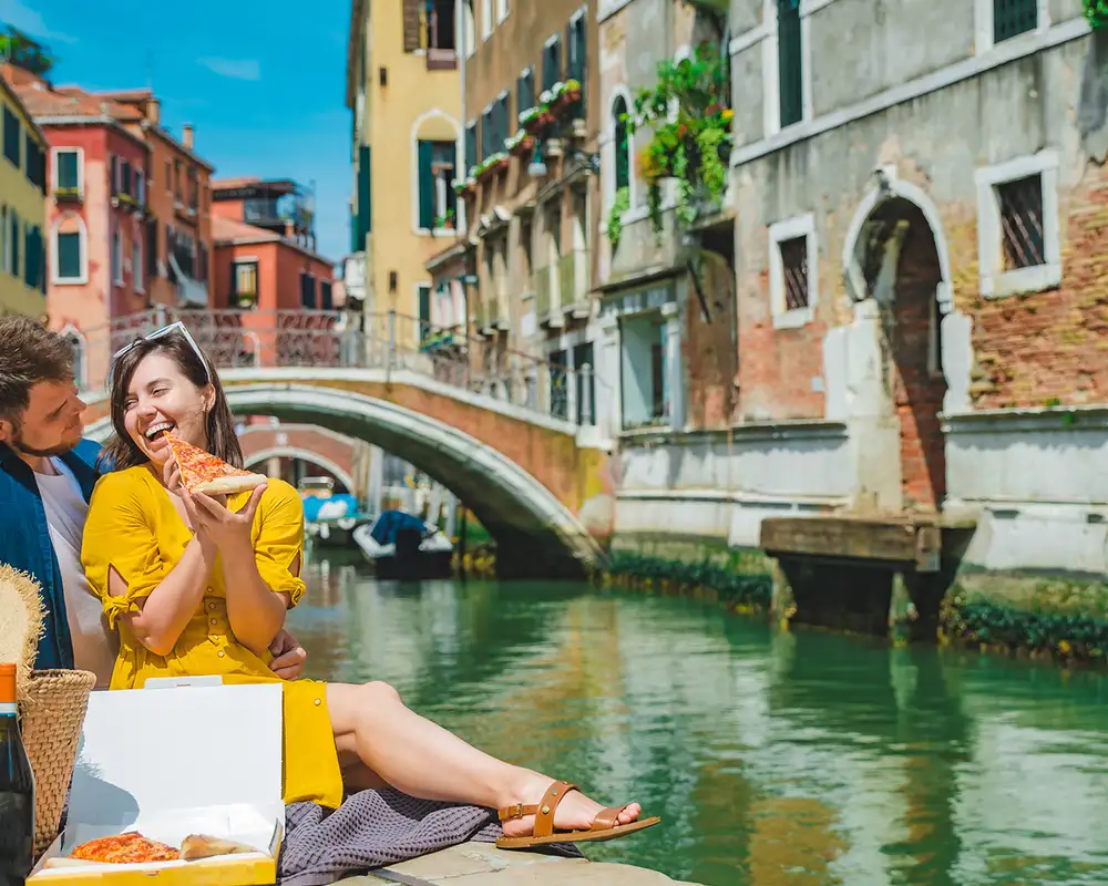 A Couple eating pizza next to the canals of Venice