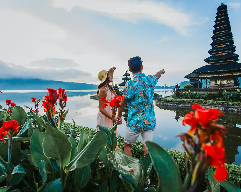 A couple standing next to some red flowers and pointing towards a building in Bali