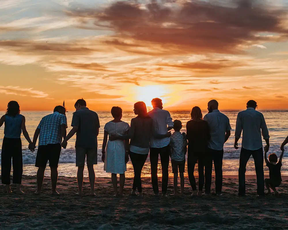 A large family standing by the shore at sunset