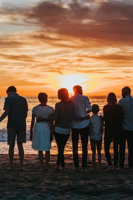 A large family standing by the shore at sunset