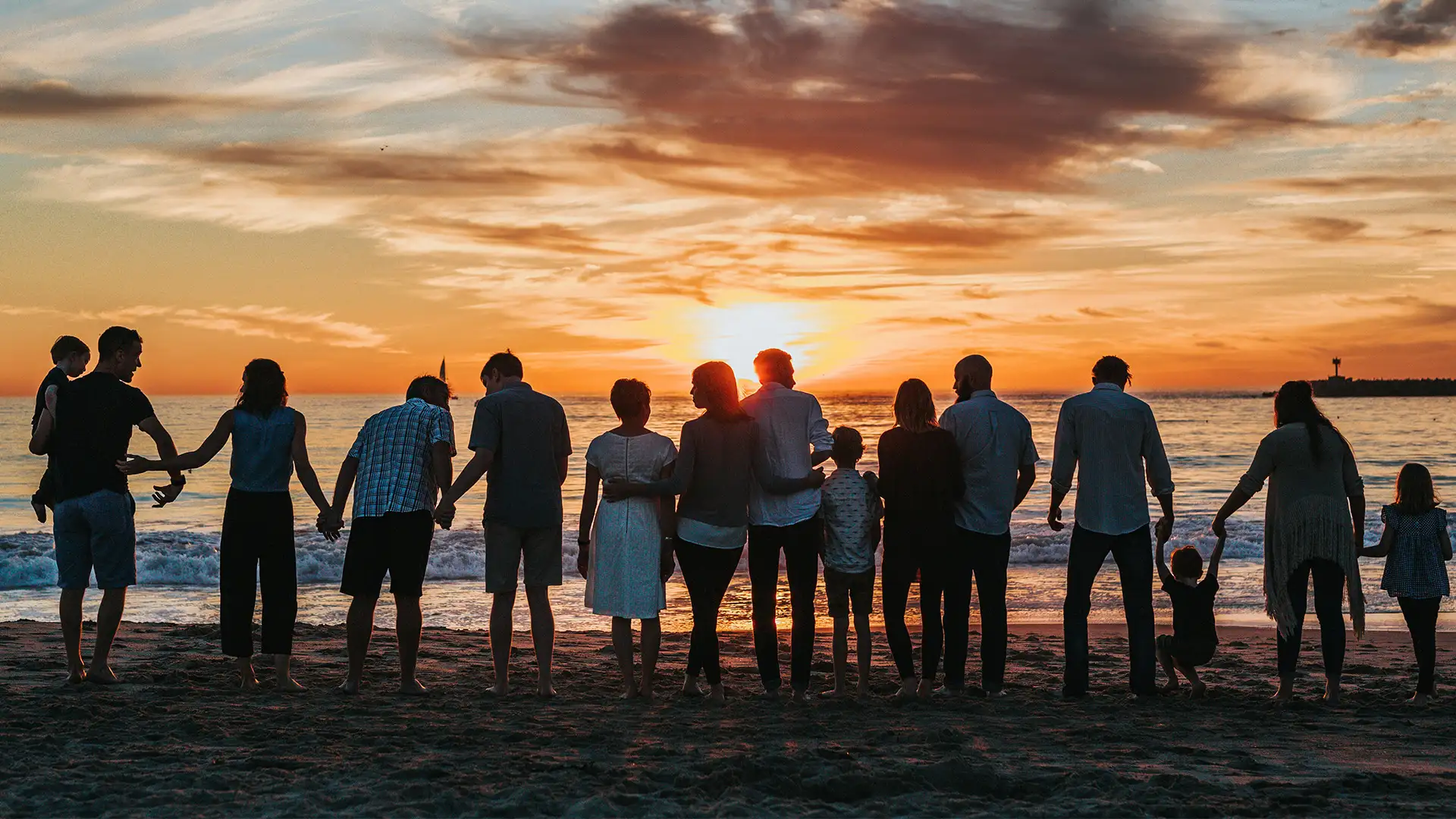 A large family standing by the shore at sunset