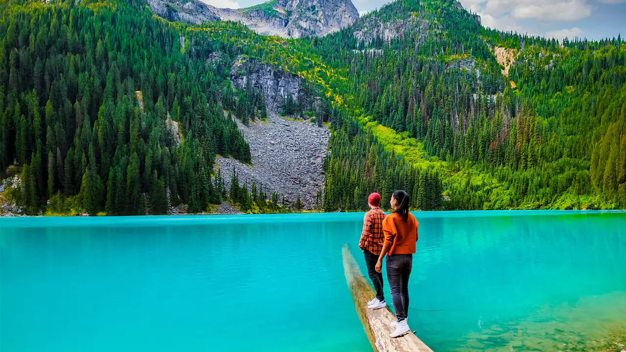 A couple walking on a log looking over Joffre Lake in Canada